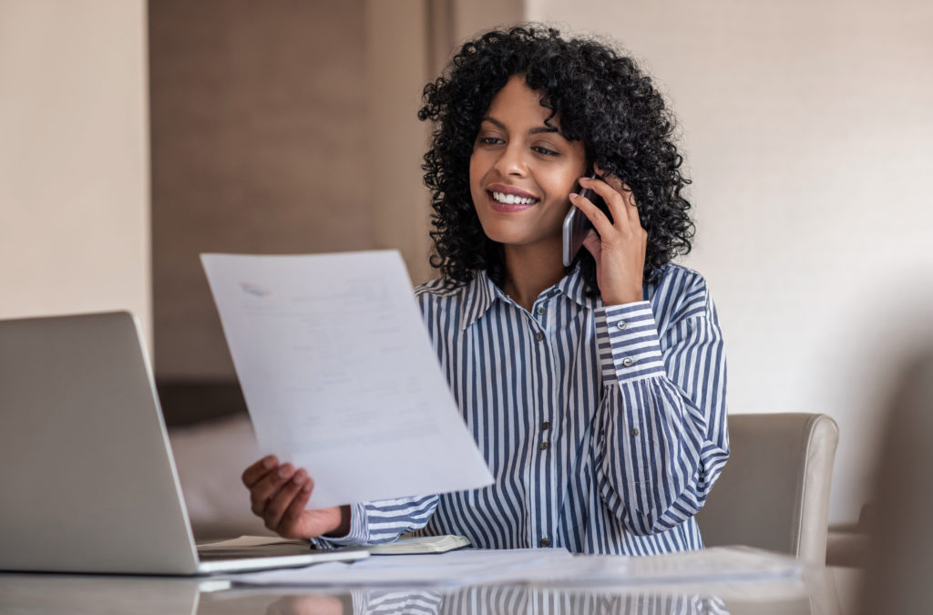 Smiling female property manager talking on her cellphone and reading documents during a customer service call